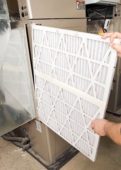 A person replacing a furnace filter in Addison